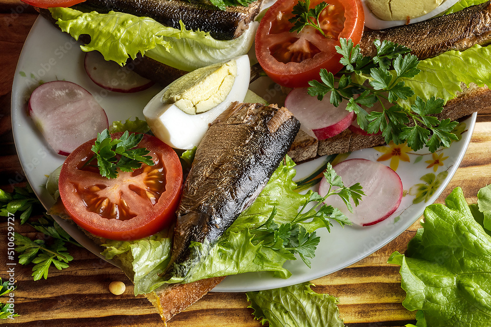 Sandwiches with sprats, eggs and vegetables lie on the plates. Dark wood background. Sandwiches with sprats, eggs and vegetables lie on the plates. Dark wood background.