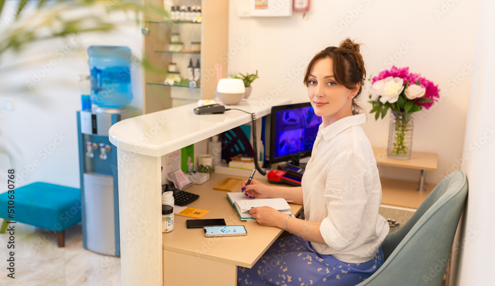 Woman Receptionist. Reception Workplace. Workplace in Beauty Salon. White Interior. White Reception Desk. Beauty Consept Woman Receptionist. Reception Workplace. Workplace in Beauty Salon. White Interior. White Reception Desk. Beauty Consept