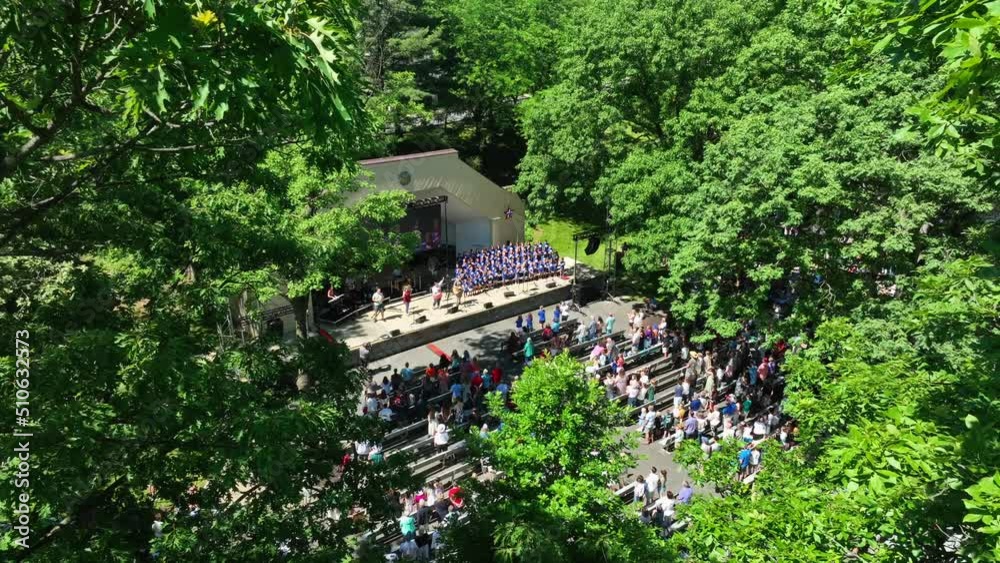 Aerial framing among trees of outdoor concert. Crowd of people gather in park for music. Aerial framing among trees of outdoor concert. Crowd of people gather in park for music.