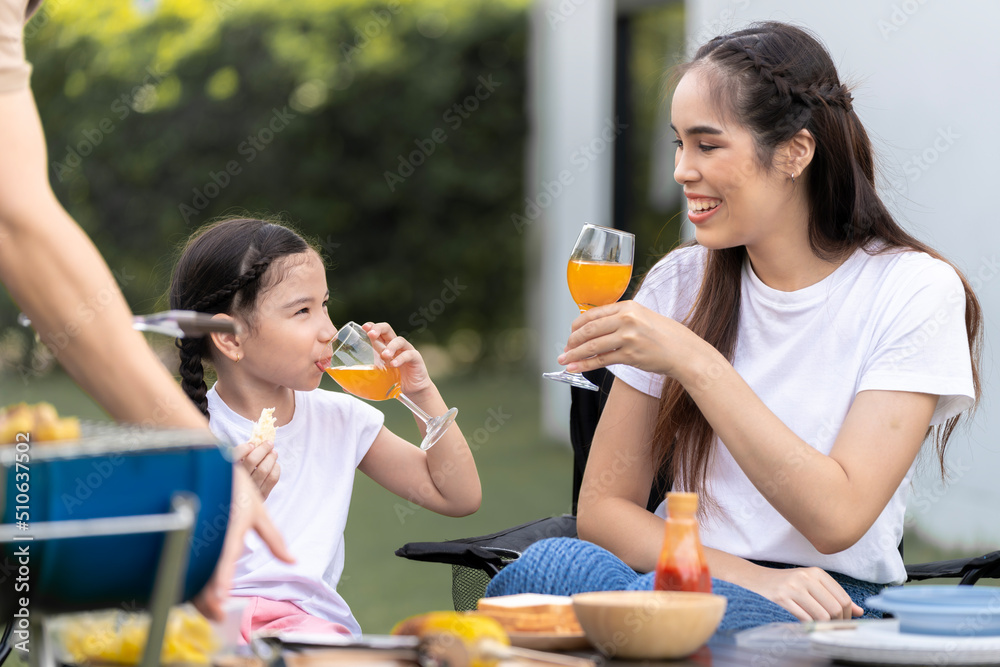 An Asian family of parents and daughters camping with BBQ tires. in the front yard outside the house together happily An Asian family of parents and daughters camping with BBQ tires. in the front yard outside the house together happily