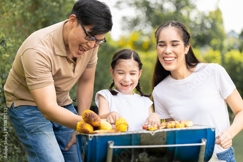 An Asian family of parents and daughters camping with BBQ tires. in the front yard outside the house together happily