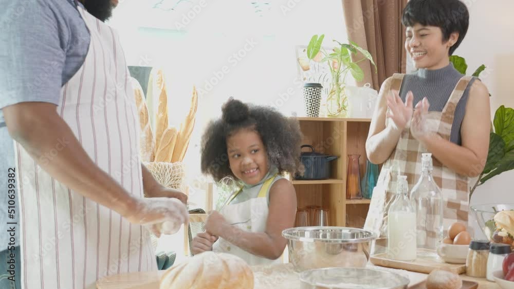 African America family wearing apron thresh flour for cooking and dancing and song together in the kitchen at home, parent and little child preparing food and song with fun and playful. African America family wearing apron thresh flour for cooking and dancing and song together in the kitchen at home, parent and little child preparing food and song with fun and playful.