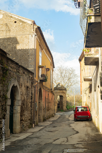 Fototapeta Naklejka Na Ścianę i Meble -  Narrow historic (medieval) streets of a small town in southern Italy. Old stone houses, wooden windows and doors, cobblestone road.