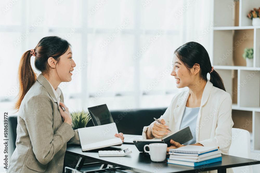 Young beautiful asian business woman is talking to her colleague, while sitting at the desk in a modern office. Concept of business success. Young beautiful asian business woman is talking to her colleague, while sitting at the desk in a modern office. Concept of business success.