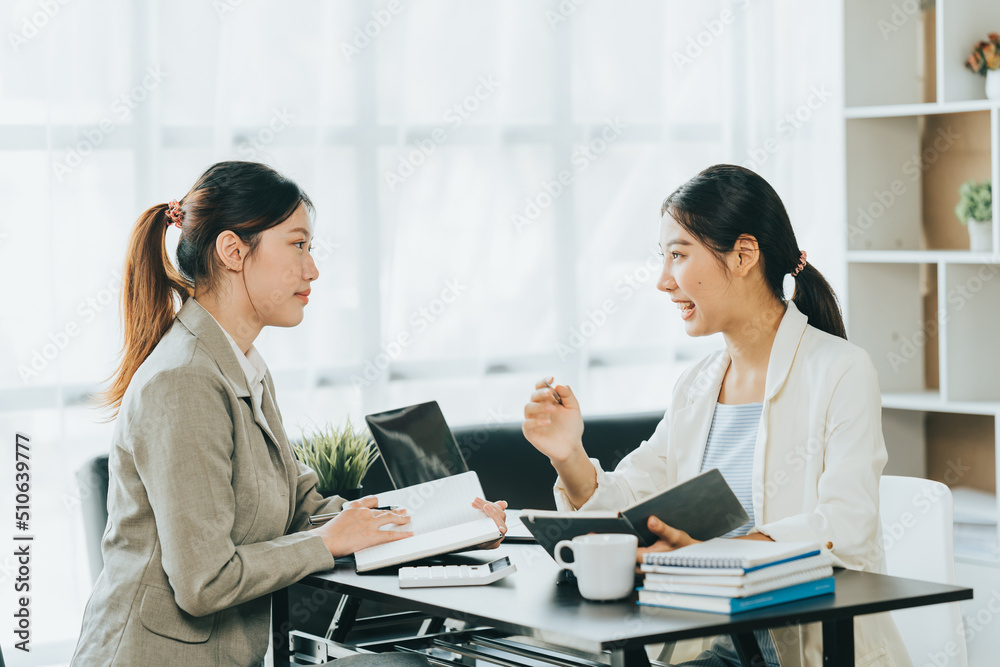 Young beautiful asian business woman is talking to her colleague, while sitting at the desk in a modern office. Concept of business success. Young beautiful asian business woman is talking to her colleague, while sitting at the desk in a modern office. Concept of business success.