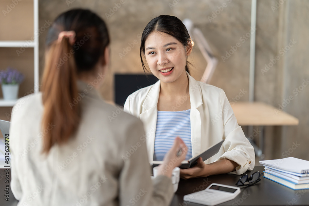 Young beautiful asian business woman is talking to her colleague, while sitting at the desk in a modern office. Concept of business success. Young beautiful asian business woman is talking to her colleague, while sitting at the desk in a modern office. Concept of business success.