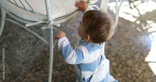 Cute baby toddler learning to stand up by leaning on chair furniture