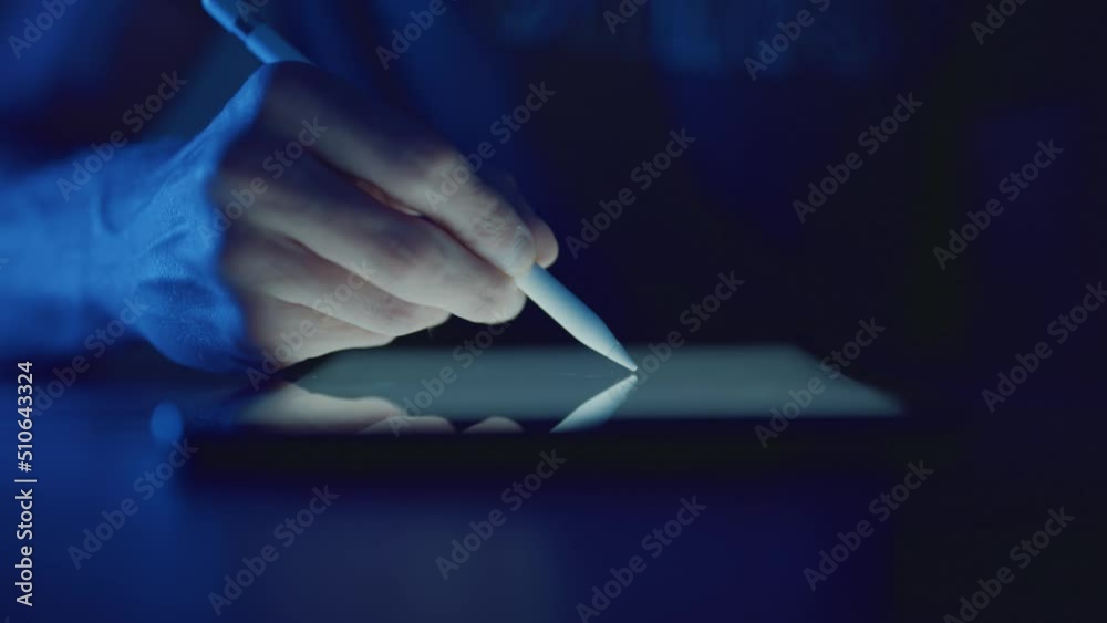 Designer sketching with digital stylus on glowing graphics tablet at night