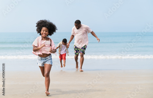 Happy African American kid girl run with family on the beach