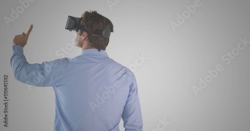 Caucasian man wearing vr headset touching an invisible screen against copy space on grey background