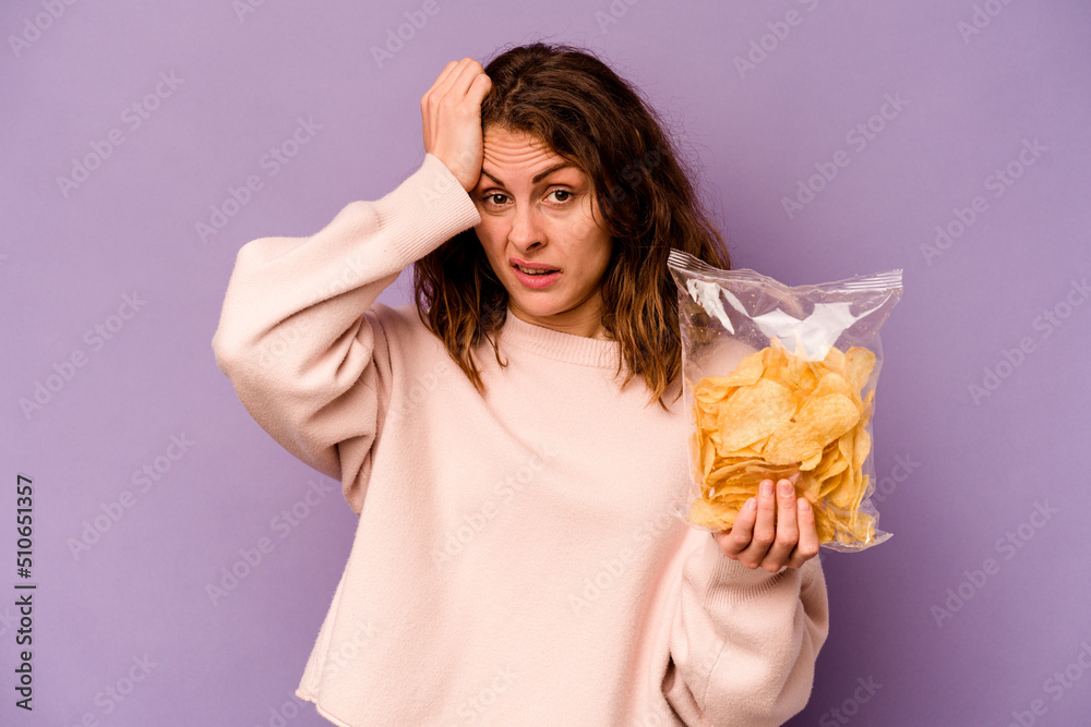Young caucasian woman holding a bag of chips isolated on purple background being shocked, she has remembered important meeting. Young caucasian woman holding a bag of chips isolated on purple background being shocked, she has remembered important meeting.