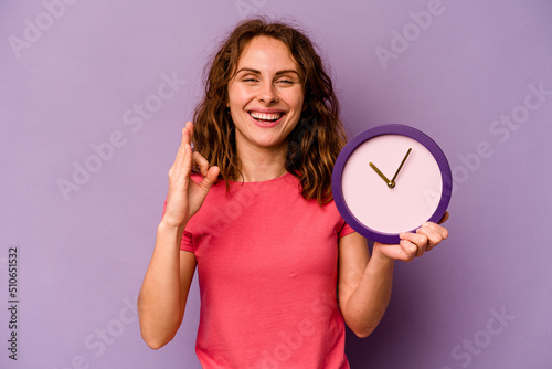 Young caucasian woman holding a clock isolated on yellow background cheerful and confident showing ok gesture. photo