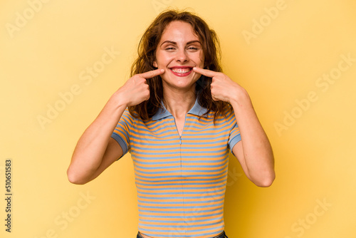 Young caucasian woman isolated on yellow background smiles, pointing fingers at mouth.