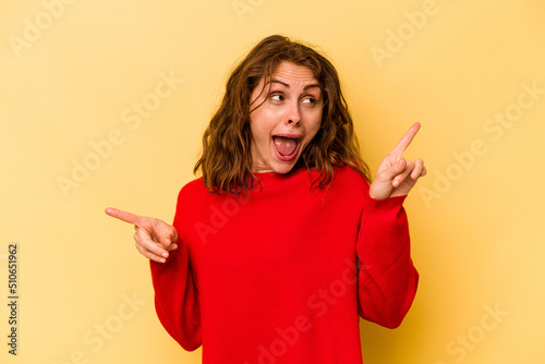 Young caucasian woman isolated on yellow background pointing to different copy spaces, choosing one of them, showing with finger.