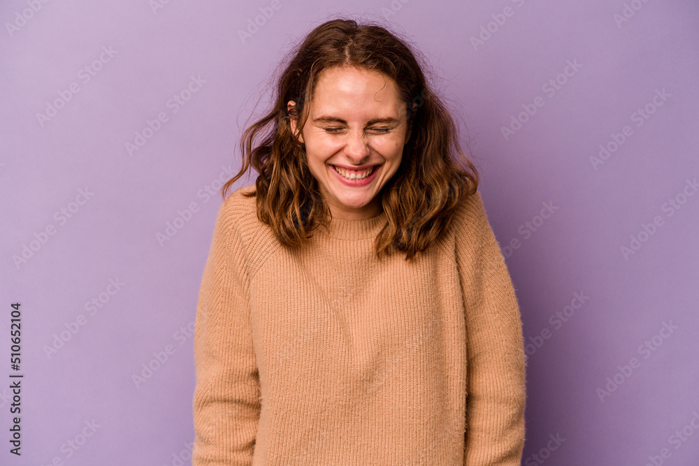 Fototapeta premium Young caucasian woman isolated on purple background laughs and closes eyes, feels relaxed and happy.