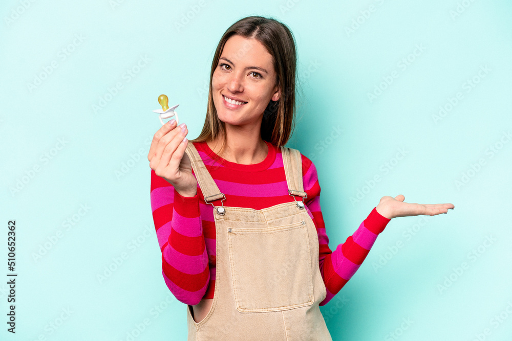 Young caucasian pregnant woman isolated on blue background showing a copy space on a palm and holding another hand on waist. Young caucasian pregnant woman isolated on blue background showing a copy space on a palm and holding another hand on waist.