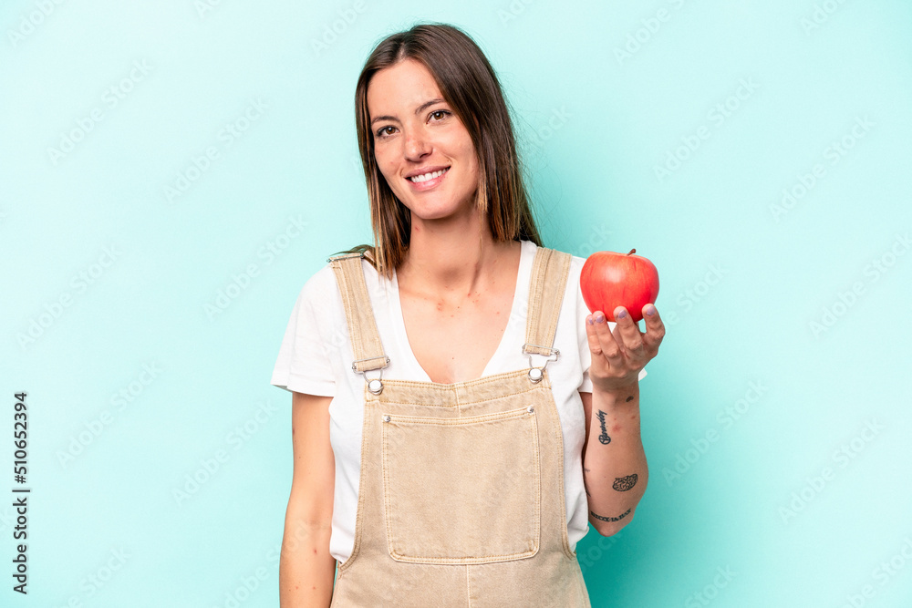 Young caucasian pregnant woman holding an apple isolated on blue background happy, smiling and cheerful. Young caucasian pregnant woman holding an apple isolated on blue background happy, smiling and cheerful.