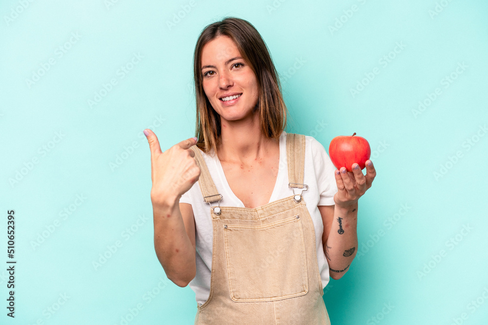 Young caucasian pregnant woman holding an apple isolated on blue background pointing with finger at you as if inviting come closer. Young caucasian pregnant woman holding an apple isolated on blue background pointing with finger at you as if inviting come closer.
