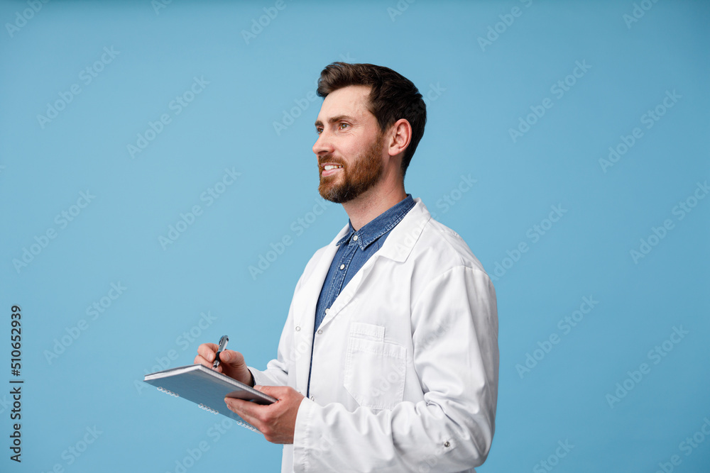 Doctor making medical notes in clipboard standing over blue studio background