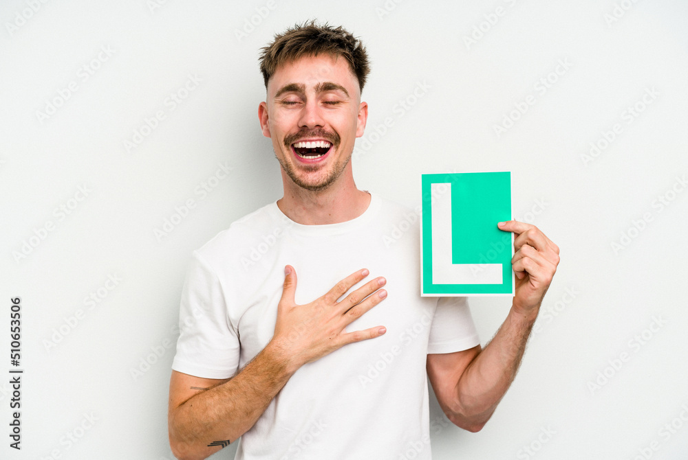 Young caucasian man holding L placard isolated on white background laughs out loudly keeping hand on chest.