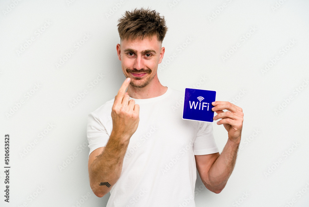 Young caucasian man holding wifi placard isolated on white background pointing with finger at you as if inviting come closer. Young caucasian man holding wifi placard isolated on white background pointing with finger at you as if inviting come closer.