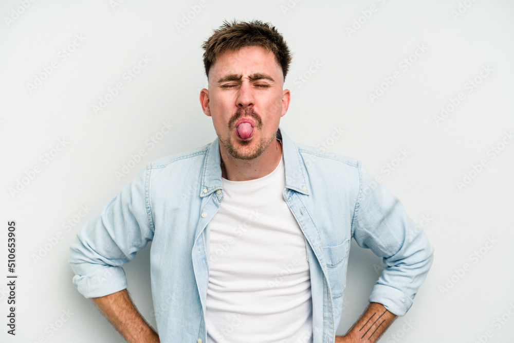 Fototapeta premium Young caucasian man isolated on white background funny and friendly sticking out tongue.