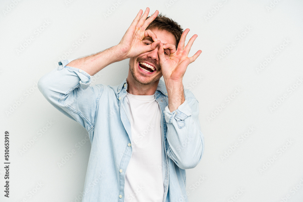 Young caucasian man isolated on white background showing okay sign over eyes Young caucasian man isolated on white background showing okay sign over eyes