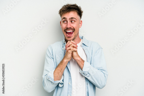 Young caucasian man isolated on white background keeps hands under chin, is looking happily aside.