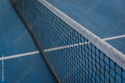 Close up of nylon tennis net across a blue court.