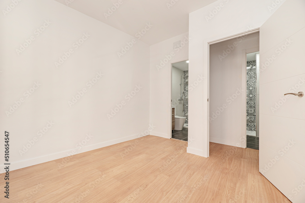 Empty room with two access doors to bathrooms, oak parquet floor and plain white painted walls Empty room with two access doors to bathrooms, oak parquet floor and plain white painted walls