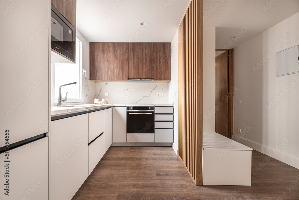 Front of a kitchen with white wooden furniture combined with wood-colored furniture and white marble wall, wooden floors and black appliances Front of a kitchen with white wooden furniture combined with wood-colored furniture and white marble wall, wooden floors and black appliances