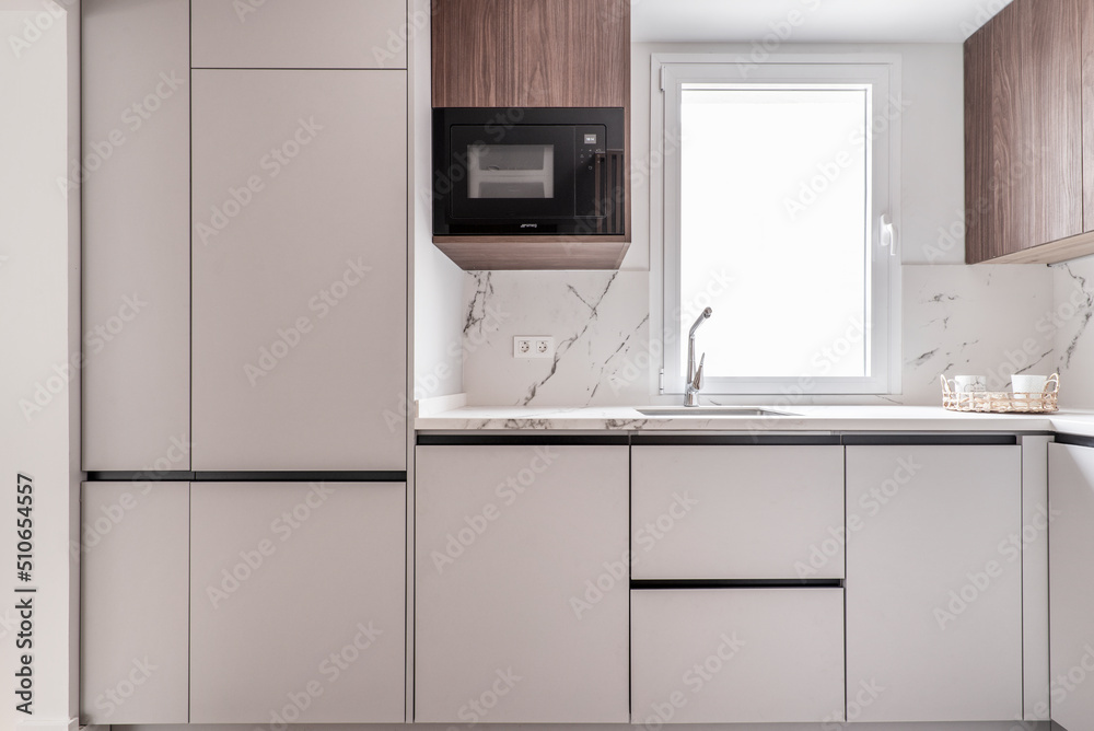 Front of a kitchen with white wooden furniture combined with wood-colored furniture, white marble walls and white aluminum window Front of a kitchen with white wooden furniture combined with wood-colored furniture, white marble walls and white aluminum window