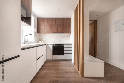 Front of a kitchen with white wooden furniture combined with wood-colored furniture and white marble wall, wooden floors and black appliances photo