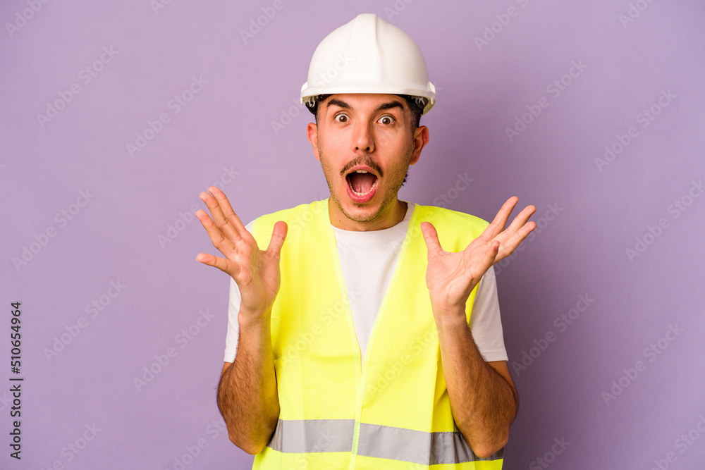 Young hispanic worker man isolated on purple background surprised and shocked. Young hispanic worker man isolated on purple background surprised and shocked.