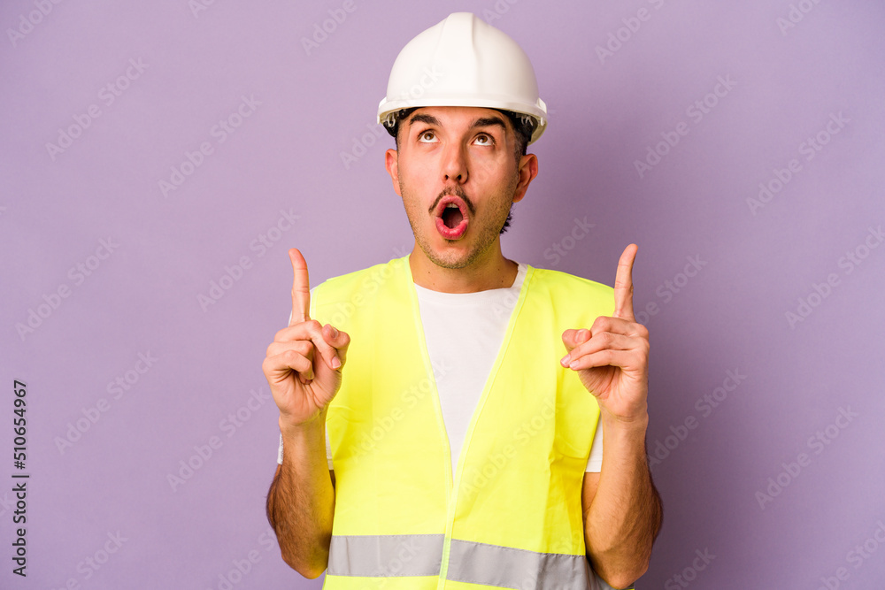 Young hispanic worker man isolated on purple background pointing upside with opened mouth.
