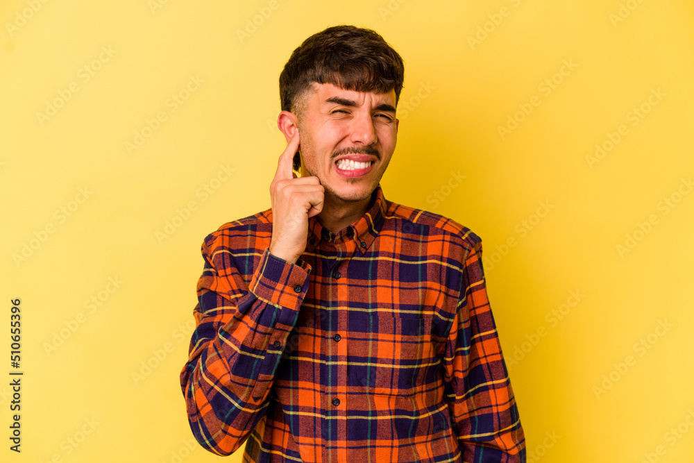 Young caucasian man isolated on yellow background covering ears with fingers, stressed and desperate by a loudly ambient. Young caucasian man isolated on yellow background covering ears with fingers, stressed and desperate by a loudly ambient.