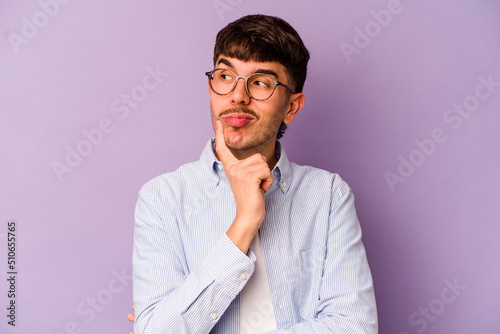 Young caucasian man isolated on purple background contemplating, planning a strategy, thinking about the way of a business.