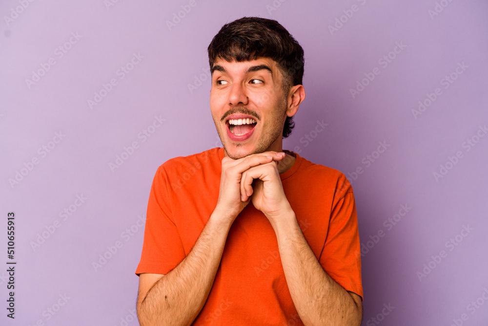 Young caucasian man isolated on purple background keeps hands under chin, is looking happily aside. Young caucasian man isolated on purple background keeps hands under chin, is looking happily aside.
