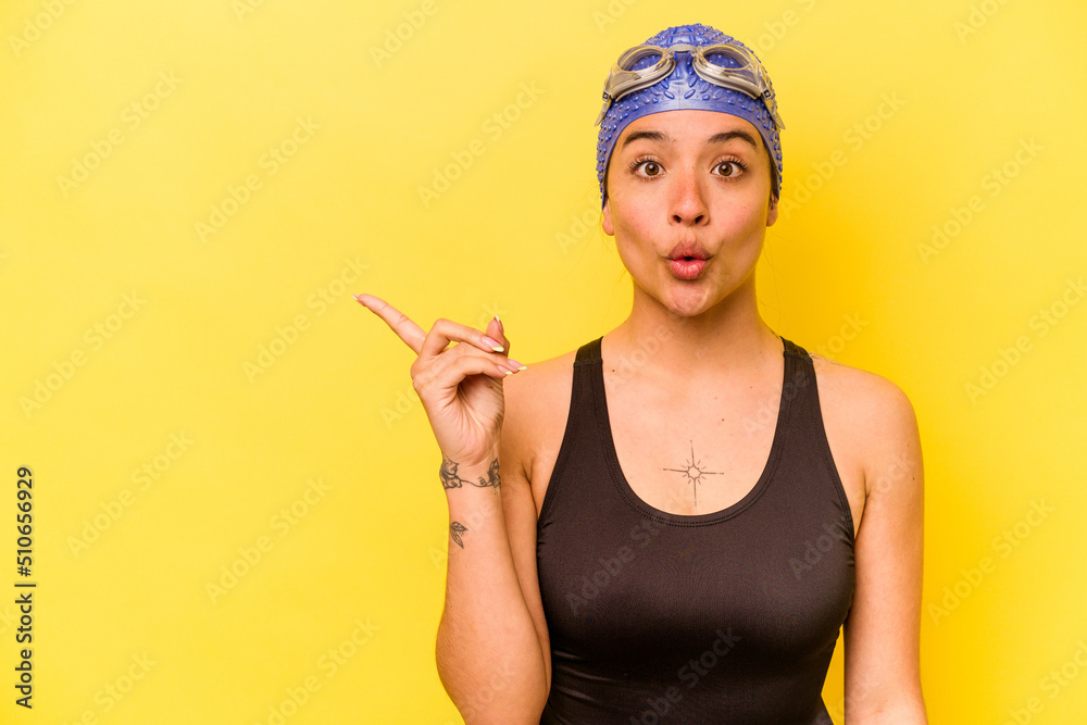 Young swimmer hispanic woman isolated on yellow background pointing to the side Young swimmer hispanic woman isolated on yellow background pointing to the side