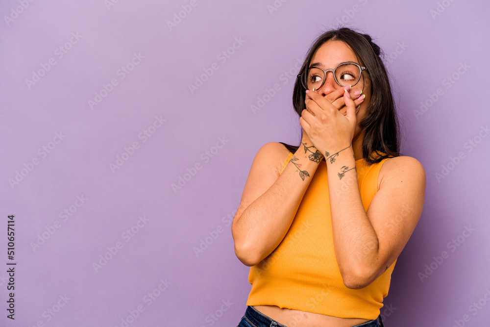 Young hispanic woman isolated on purple background thoughtful looking to a copy space covering mouth with hand. Young hispanic woman isolated on purple background thoughtful looking to a copy space covering mouth with hand.