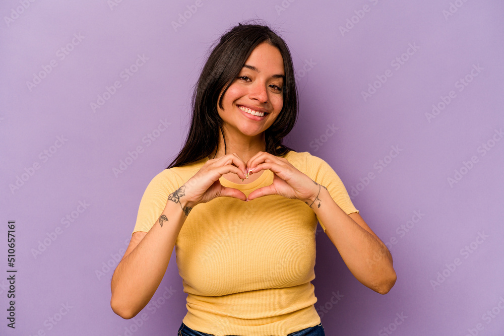 Young hispanic woman isolated on purple background smiling and showing a heart shape with hands. Young hispanic woman isolated on purple background smiling and showing a heart shape with hands.