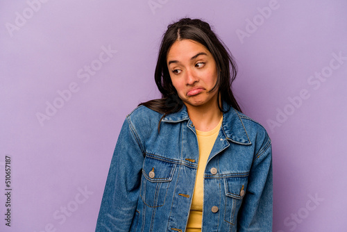 Young hispanic woman isolated on purple background shrugs shoulders and open eyes confused. © Asier