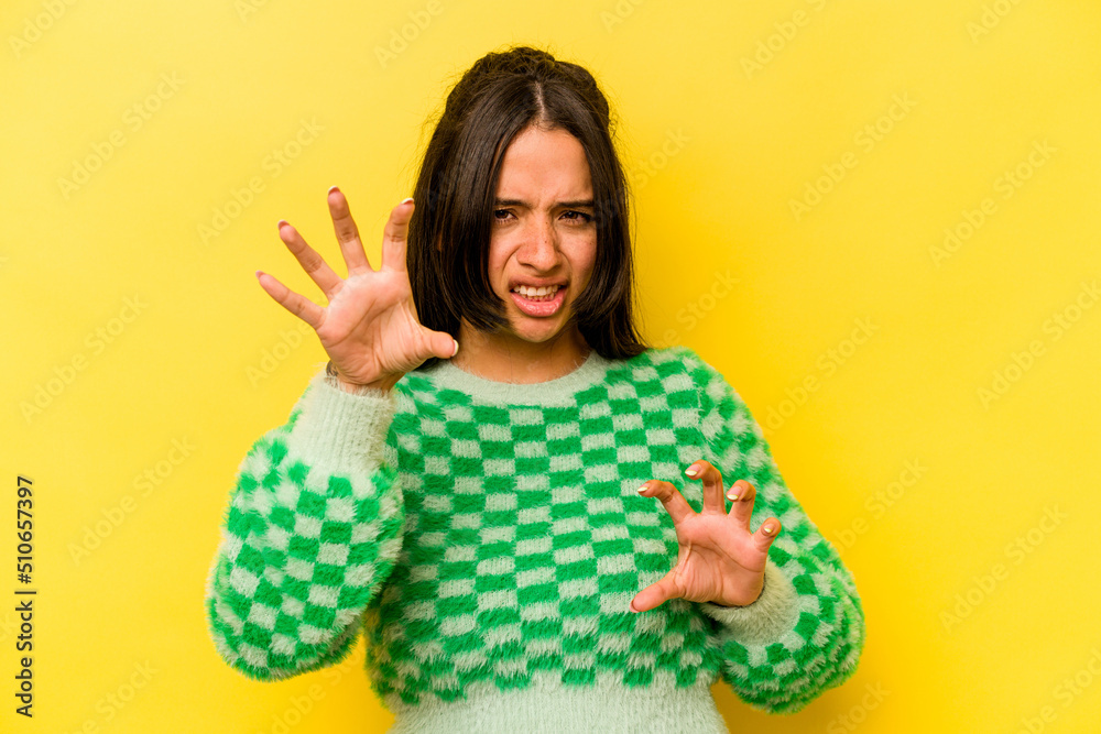 Young hispanic woman isolated on yellow background showing claws imitating a cat, aggressive gesture. Young hispanic woman isolated on yellow background showing claws imitating a cat, aggressive gesture.