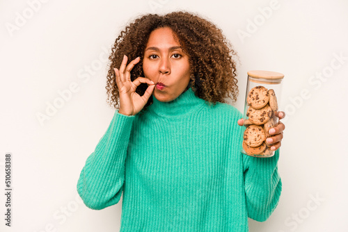 Young African American woman holding a cookies jar isolated on white background with fingers on lips keeping a secret. photo