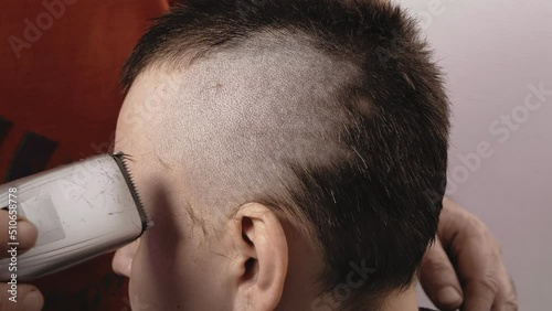 A man barber shaves a woman with a machine leaving a mohawk. Close-up photo