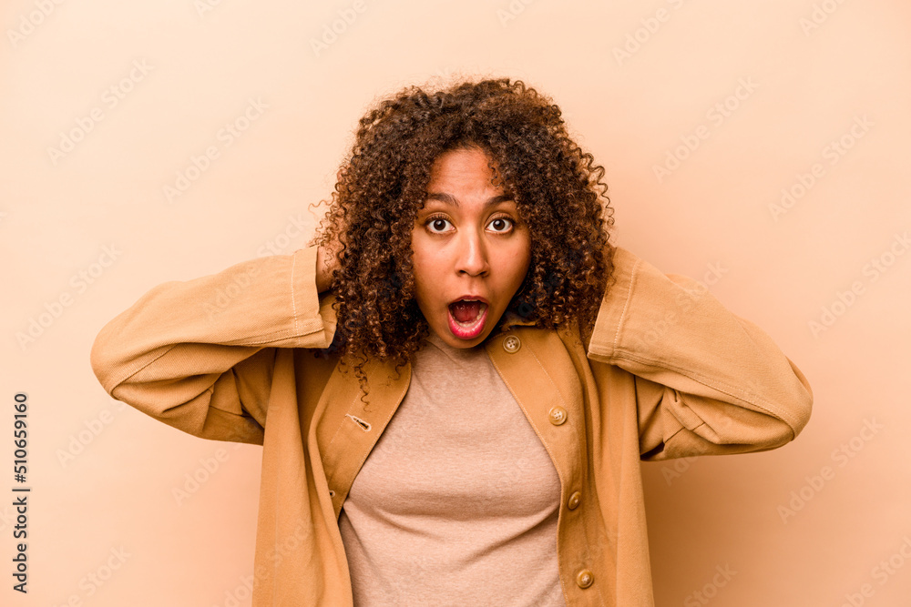 Young African American woman isolated on beige background screaming, very excited, passionate, satisfied with something. Young African American woman isolated on beige background screaming, very excited, passionate, satisfied with something.