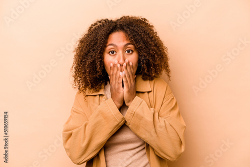 Young African American woman isolated on beige background covering mouth with hands looking worried.