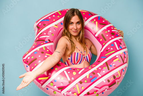 Young caucasian woman holding air mattress isolated on blue background