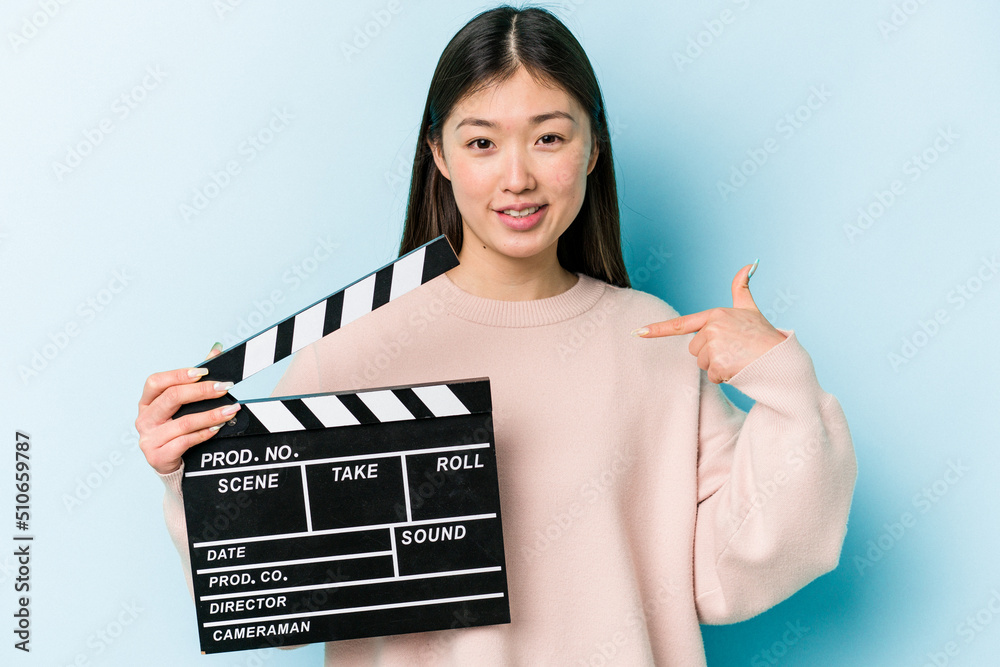Young asian woman holding clapperboard isolated on blue background person pointing by hand to a shirt copy space, proud and confident Young asian woman holding clapperboard isolated on blue background person pointing by hand to a shirt copy space, proud and confident