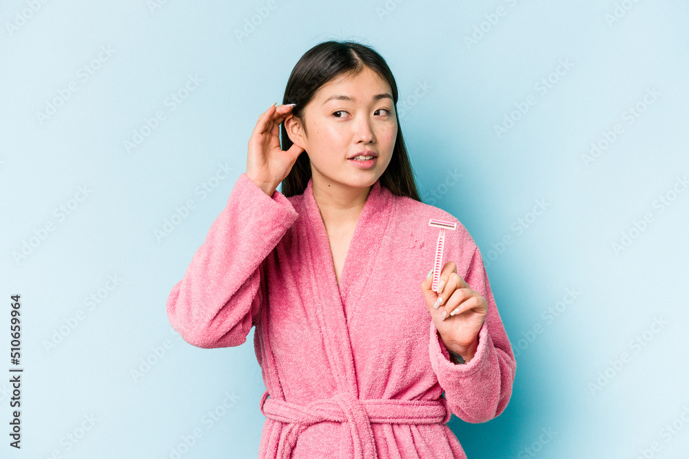 Young asian woman holding razor blade isolated on blue background trying to listening a gossip. Young asian woman holding razor blade isolated on blue background trying to listening a gossip.